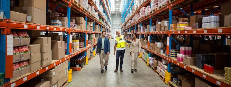A worker shows two visitors in suits around a warehouse