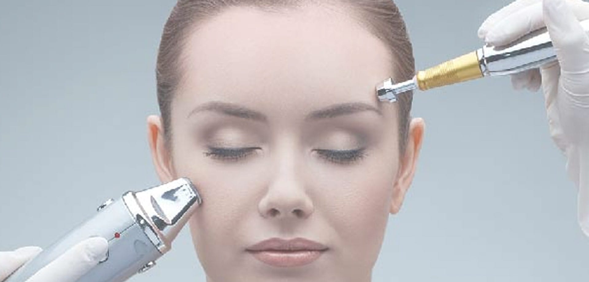 laser-by-aleya-background-1 Close-up of a person receiving a facial treatment with handheld skincare devices near the forehead and cheek