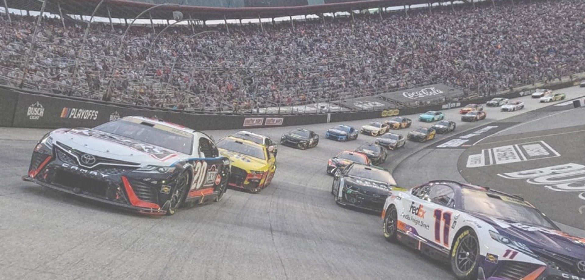 nascar-background-1 Stock cars racing in a pack on a banked oval track, with a full grandstand in the background