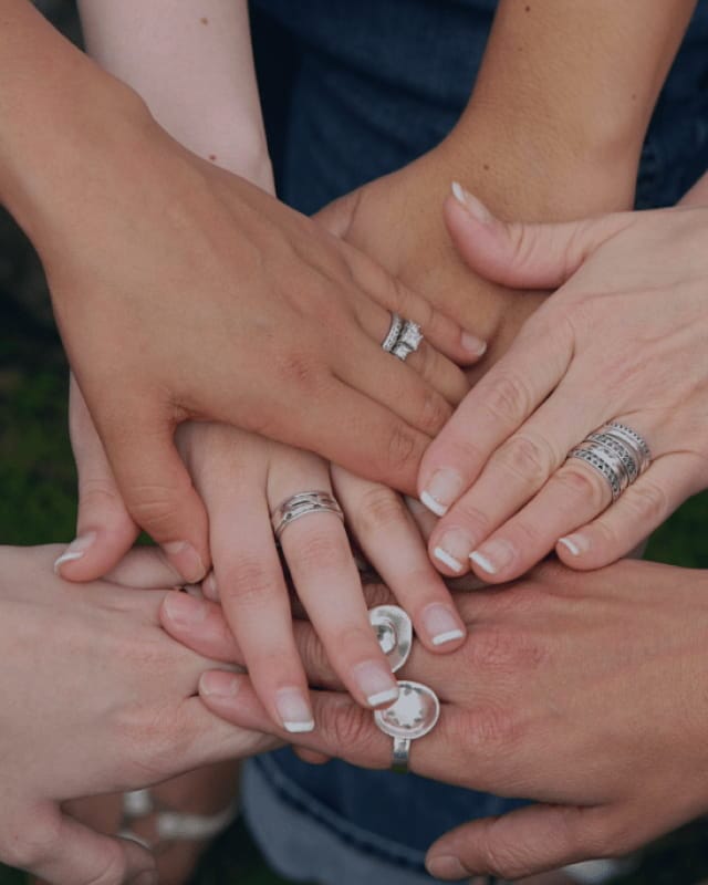 Close-up of several hands placed together, each wearing different silver and diamond rings and bands.