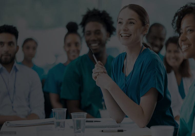 digital-marketing-agency-dental Smiling healthcare workers seated together in a group discussion, with one woman in scrubs holding a pen and speaking.