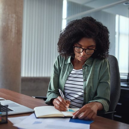 SEO specialist taking notes while reviewing campaign ideas and website strategy at a desk